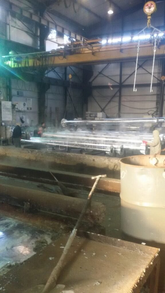 부식을 원천 차단하기 위해 탈지 및 전처리 과정을 거쳐 거대한 수조 위에서 대기 중인 대형 용융아연도금 지주 파이프들.