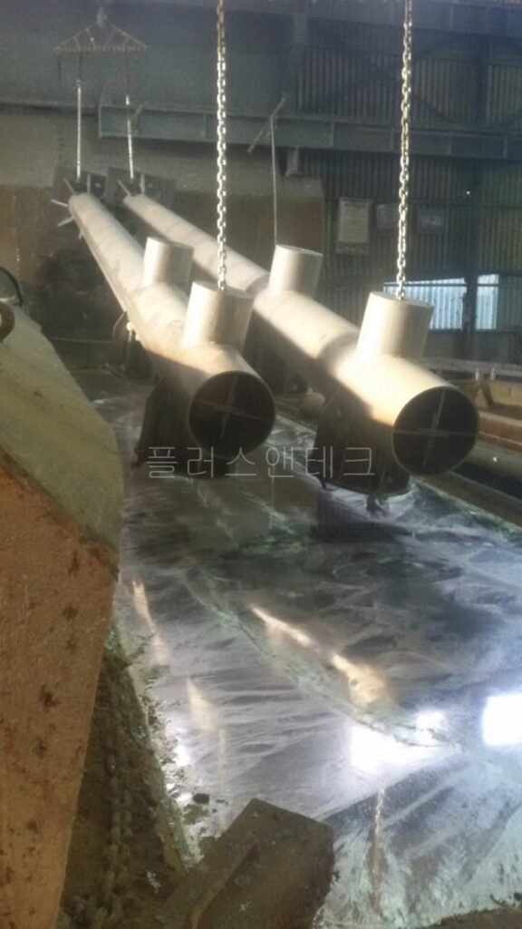 도금액에 완전히 침수되었다가 수직으로 끌어 올려져 잔여 용액을 배출하고 있는 매끄러운 은백색의 용융아연도금 지주 표면.