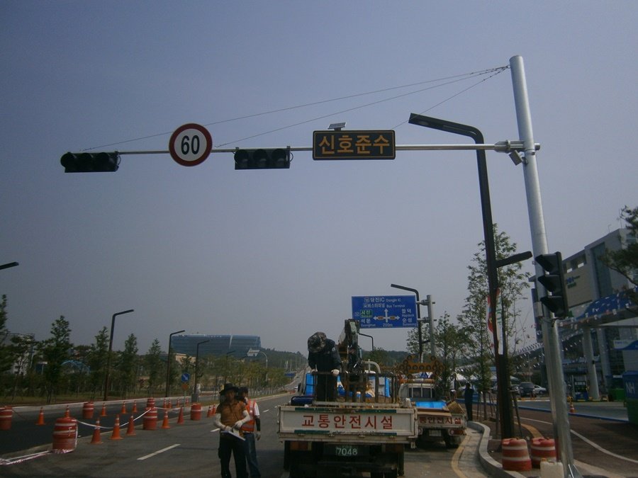 작업자가 고소작업차에 탑승하여 태양광 패널이 탑재된 신호준수 발광형 표시판을 철주에 견고하게 체결하는 정밀 시공 상세 사진.