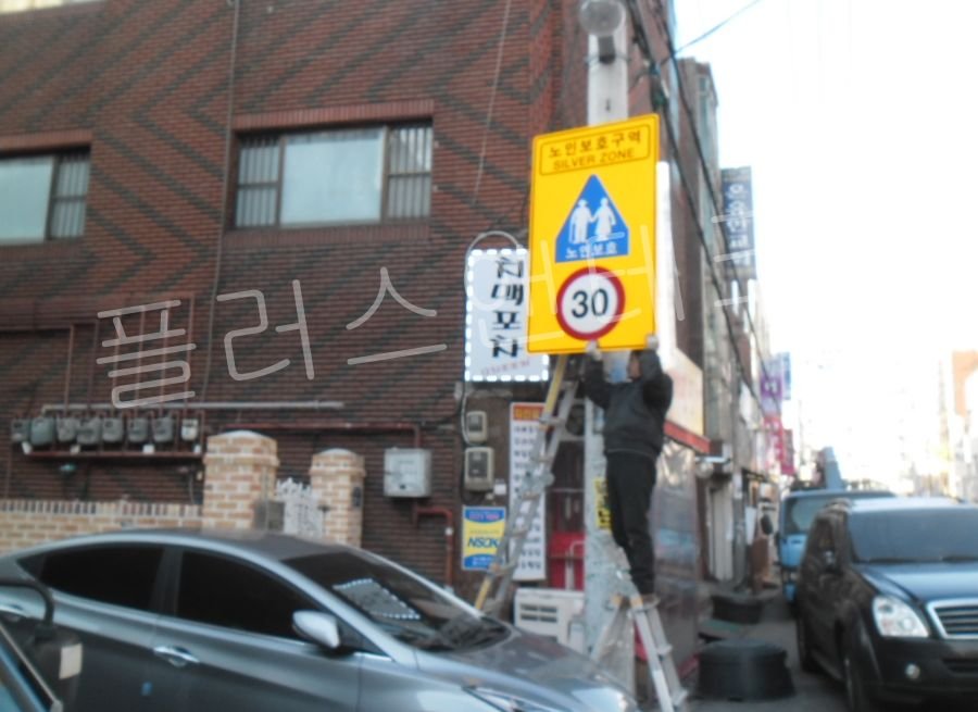 공 전문가가 사다리를 이용하여 전신주에 고강도 브라켓과 30km 제한속도 안내 노인보호표지판 설치를 세팅하는 과정.