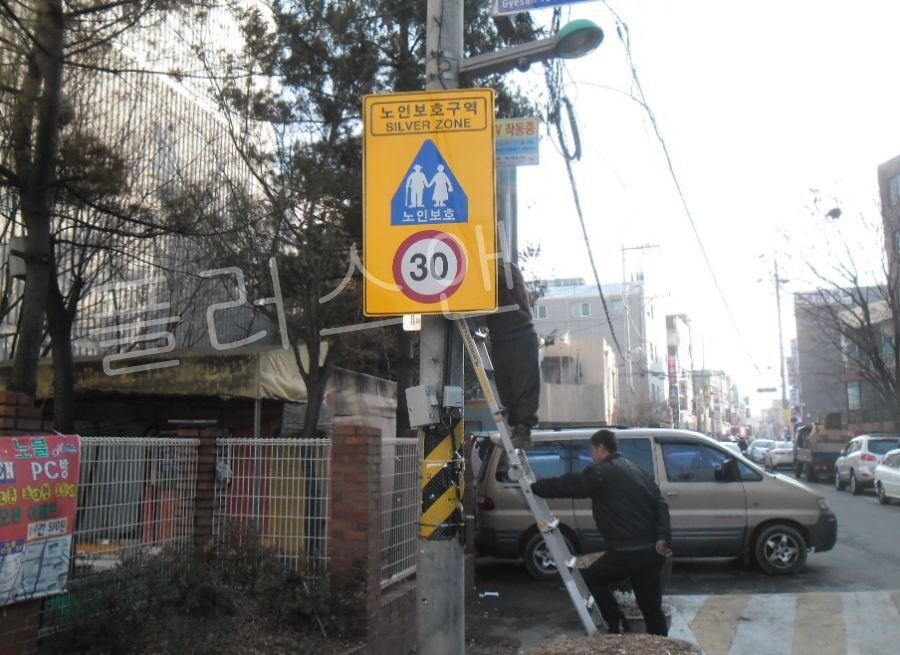 풍하중과 진동에 대비하여 스테인리스(SUS) 밴드를 팽팽하게 당겨 노인보호표지판 설치 결속을 강화하는 전문 시공 단계.