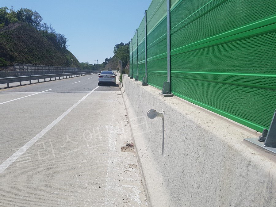 초록색 방음벽이 설치된 고속도로 방호벽 구간에 수평계 및 레벨링 작업을 거쳐 완벽한 수직(90도)으로 설치된 신규 시선유도표지