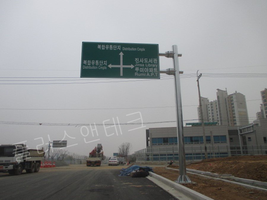 복합유통단지 내부 직진 및 좌회전 안내와 진사도서관, 루미아파트 등 인근 주거시설 우회전 방향을 동시에 표기하여 다방향 교통 흐름을 제어하는 튼튼한 도로안내표지판 전경