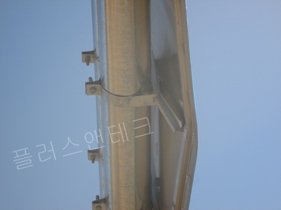 도로표지판 후면의 보강 채널과 굵은 원형 강관 지주를 견고하게 밀착시켜 고정하는 고강도 금속 밴드 및 U볼트의 정밀 체결 상태를 보여주는 측면 근접 사진