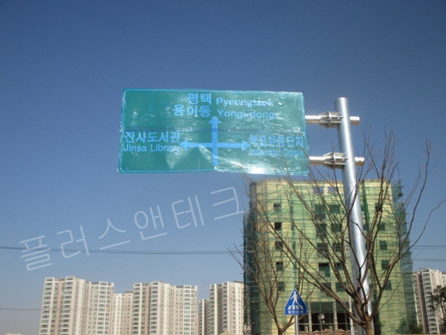 안성 복합유통단지 방향을 안내하는 대형 도로안내표지판이 지주에 결속되어 설치 완료된 모습과 주변 아파트 단지 전경