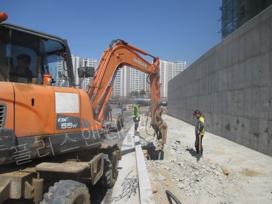  안성 복합단지 도로변에서 소형 굴삭기를 이용하여 안내표지판 지주 설치를 위한 콘크리트 경계석 인근 지반 굴착 작업을 진행하는 현장 모습