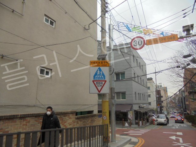 사진 도로에 위치한 기존 스쿨존 표지판 전경, 보행자가 지나가는 등 복잡한 도심지 현장의 안전 통제 전 모습