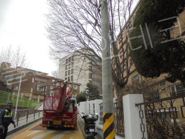 경사가 심한 스쿨존 주택가 이면도로에 고소작업차를 안전하게 주차하고 표지판 설치를 준비하는 플러스앤테크 작업자와 차량 전경