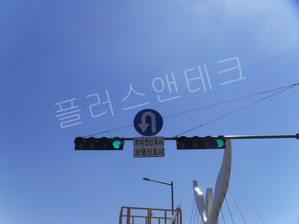 푸른 하늘을 배경으로 선명하게 점등된 녹색 화살표 좌회전 LED 신호등과 수평 지주의 견고한 결속 상태