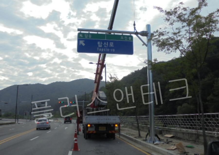 교통이 통제된 도로 위에서 크레인 장비를 이용하여 용융아연도금 처리된 대형 신규 지주를 양중하는 모습