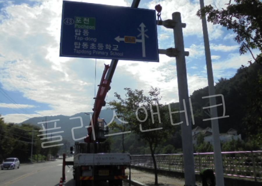  포천, 탑동, 탑동초등학교 방면을 알리는 파란색 도로표지판 상판이 크레인에 매달려 지주에 조립되는 과정