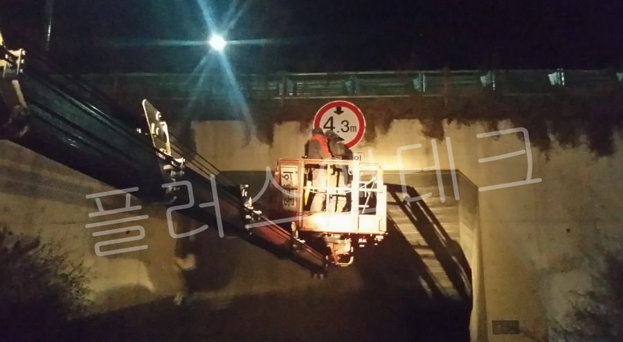투광기 조명 아래서 설치된 표지판의 수평 상태와 앵커 체결부의 견고함을 점검하는 작업자들
