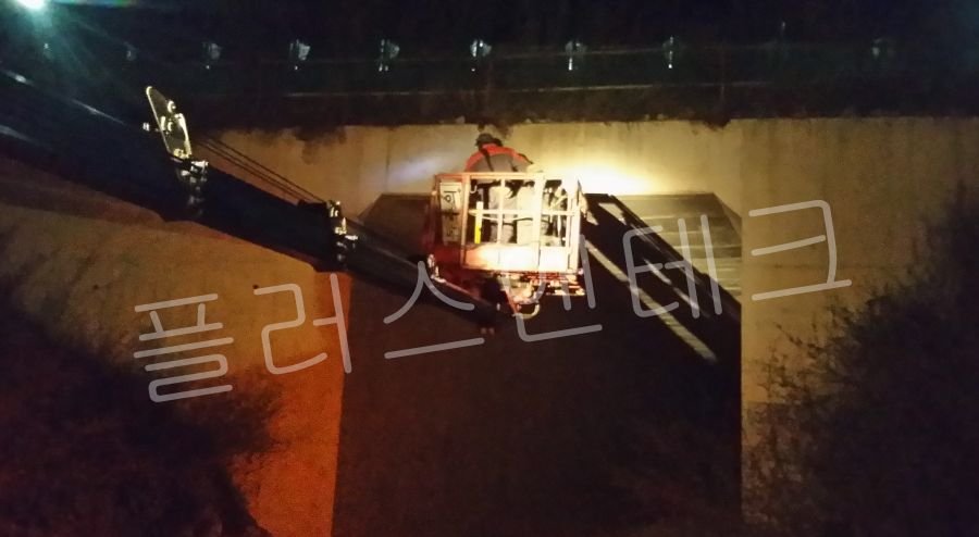 야간 도로 통제 후 고소작업차가 터널 상단 콘크리트 구조물에 접근하여 표지판 설치를 준비하는 모습