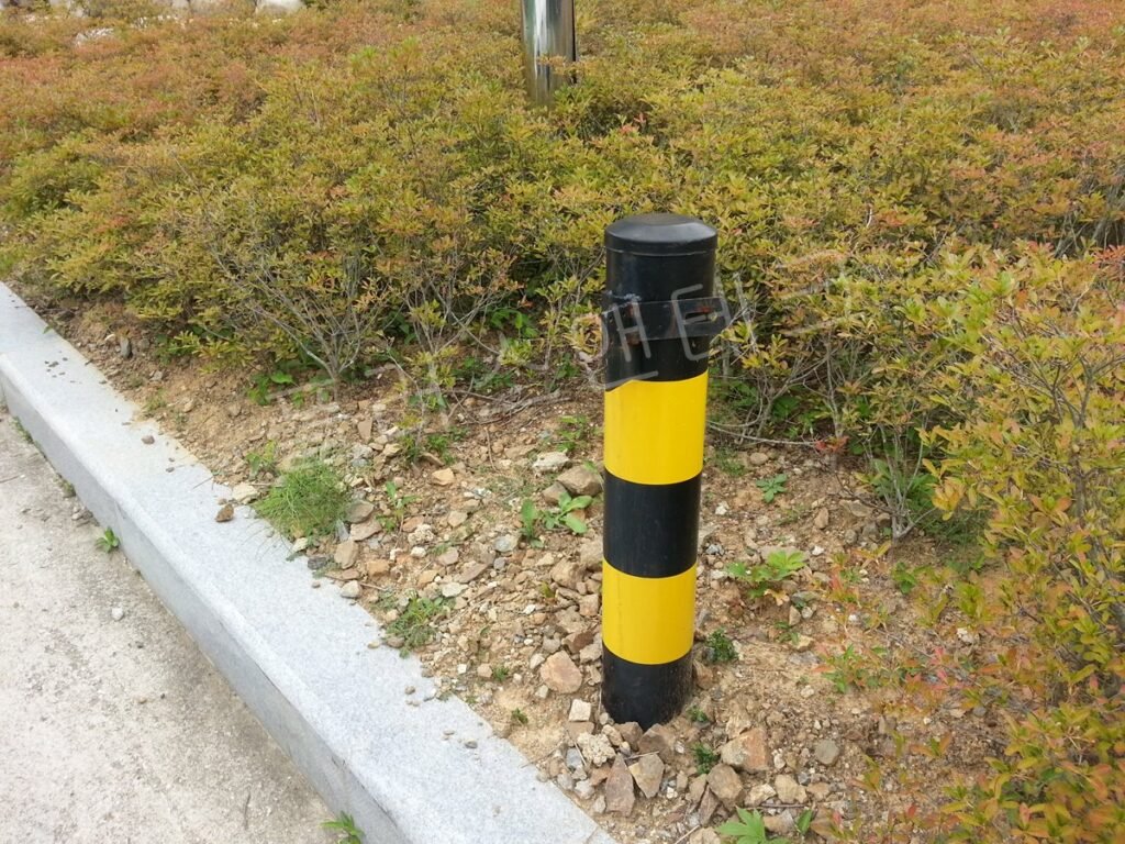 그물망 펜스 앞 잔디밭에 설치된 흑색 황색 차단기 지주와 상단 브래킷
